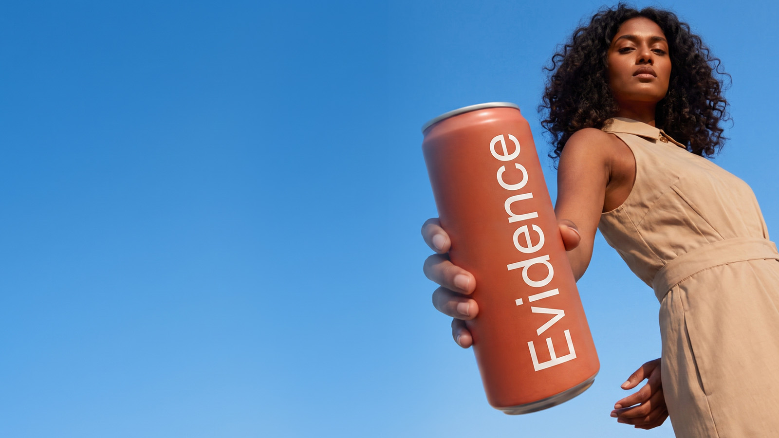 A woman holds a coral can labeled Evidence toward the viewer against a clear blue sky.