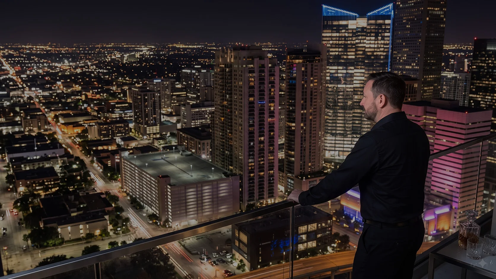 Jason George looking across an illuminated city skyline from a rooftop balcony at night.