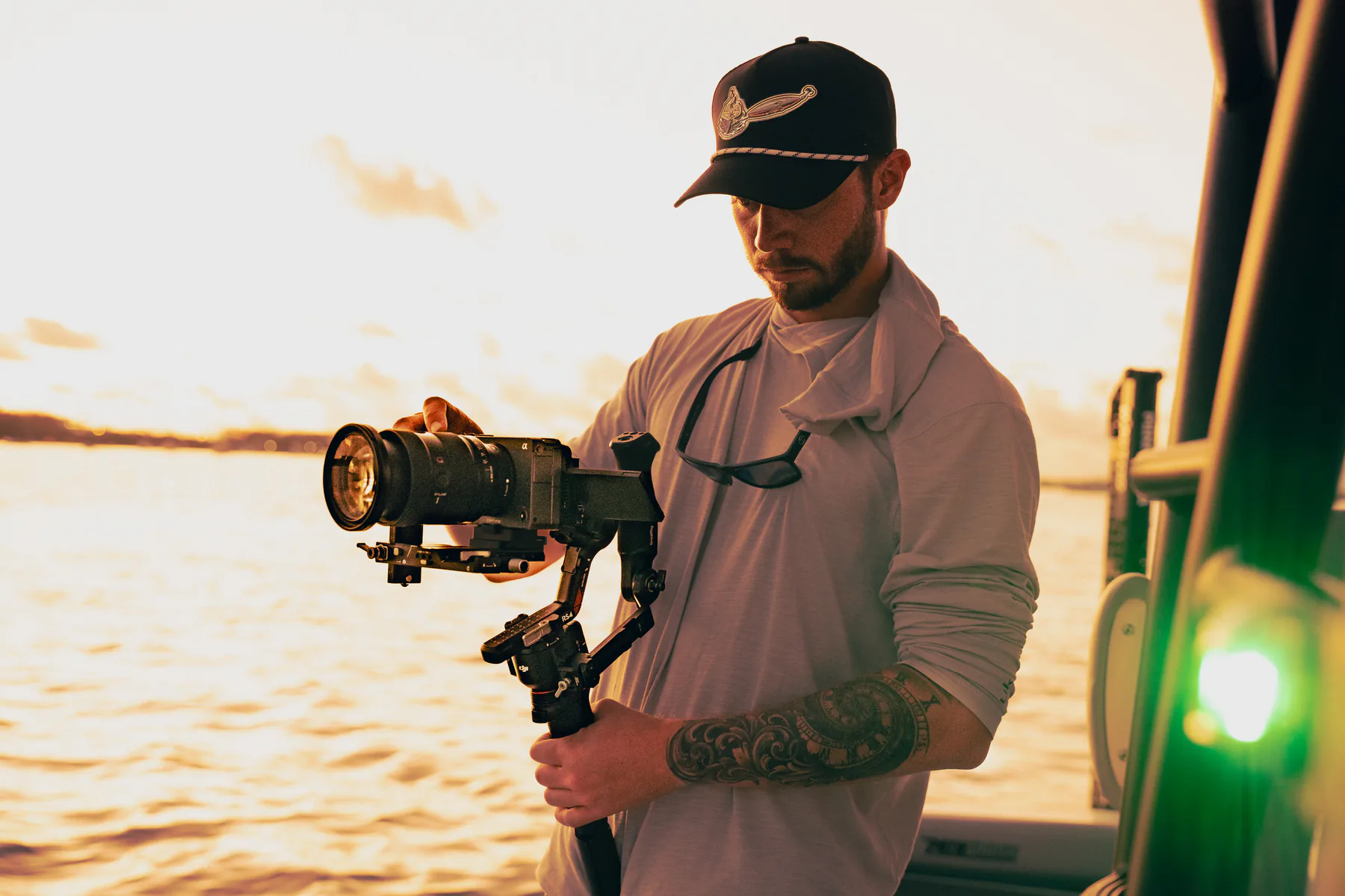 Mac Hoover balancing a cinema camera on a gimbal beside the water at sunset.