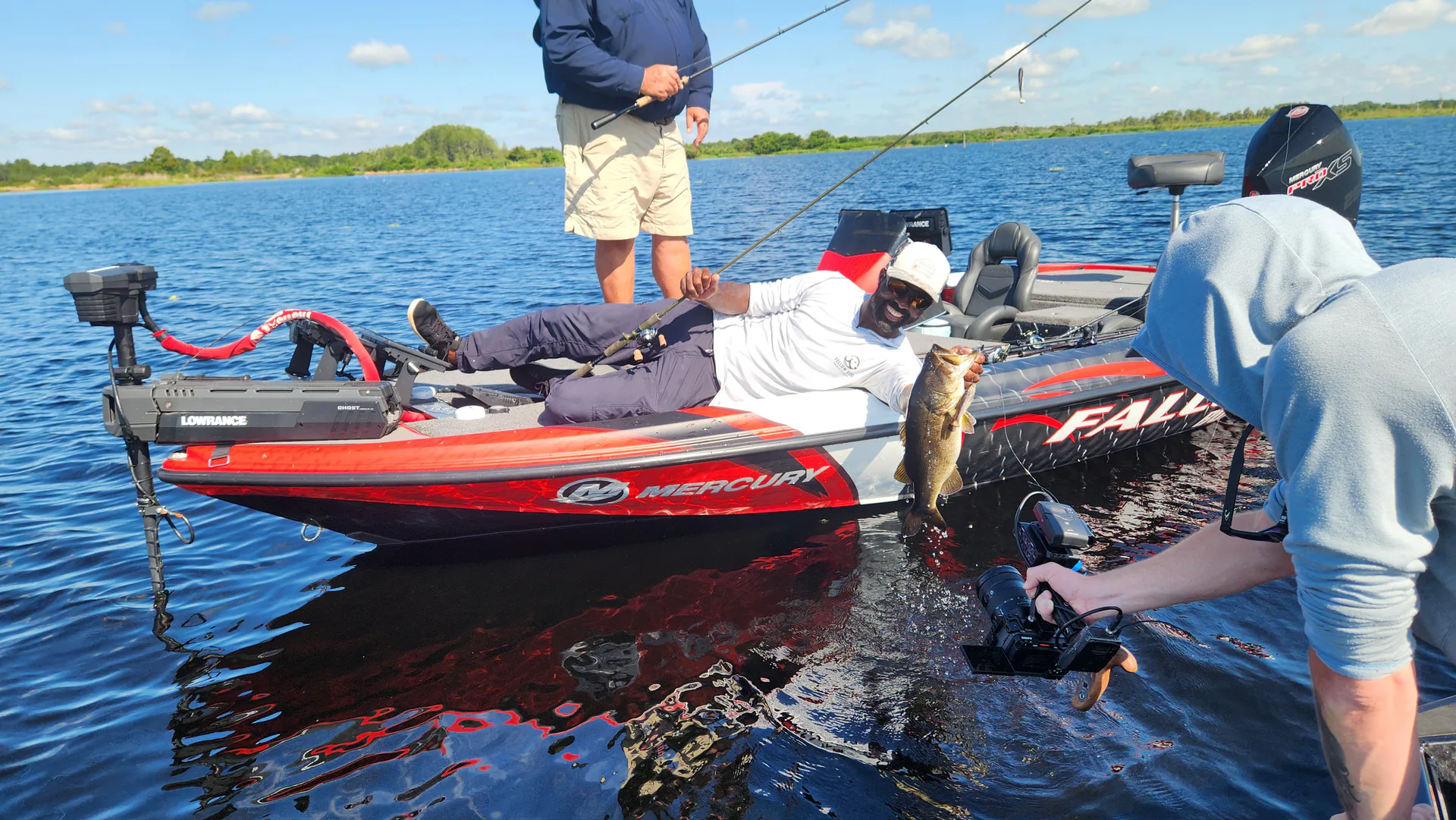 A camera operator films an angler holding a bass from a second boat during an outdoor production.